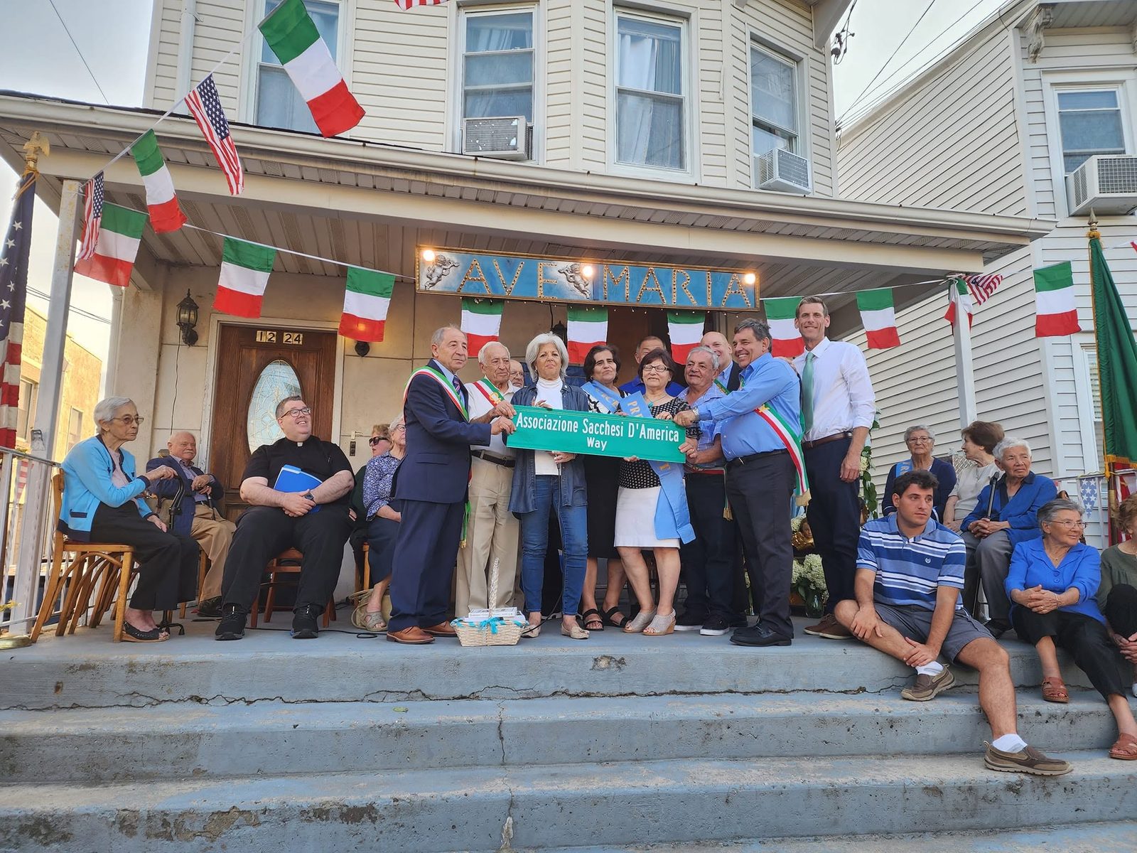 ASA leadership and members hold the Associazione Sacchesi D'America Way street sign on the steps of the clubhouse